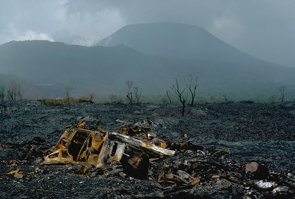 In contrast to the low profile of its neighboring shield volcano, Nyamuragira, 3470-m-high Nyiragongo displays the steep slopes of a stratovolcano.  One of Africa's most notable volcanoes, Nyiragongo contained a lava lake in its deep summit crater that was active for half a century before draining suddenly in 1977.  This January 1977 photo on the SSE flank shows a vehicle that was overrun by the extremely fluid 1977 lava flows from the draining of the summit lava lake.  The older Shaheru stratovolcano appears on the left horizon. Copyrighted photo by Katia and Maurice Krafft, 1977.