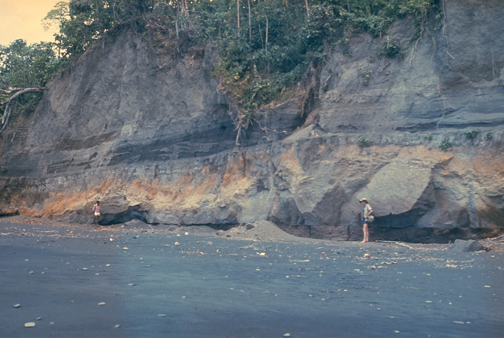 An outcrop on the W coast of Long Island reveals deposits from the last caldera-forming eruption. This catastrophic eruption in the mid-17th century deposited ash across the New Guinea highlands and prompted legends of a "Time of Darkness." This outcrop shows pyroclastic surge and Plinian airfall deposits of the Matapun formation, which is exposed at the top of the section beginning about 4 m above the geologists. Photo by Russell Blong, 1975 (Macquarie University).