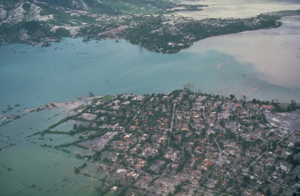 Floodwaters back up over the villages of Aglao and Dalanawan on the SW flank of Pinatubo volcano in the Philippines. Lake Mapanuepe was formed when lahars from the 1991 eruption traveled down the Marella River and dammed its tributary; several villages were submerged by the rising water. The lake was stabilized in late 1992 at about this level after excavation of a trench through bedrock, seen in the background. This prevented catastrophic rapid draining of the lake. Photo by Chris Newhall, 1991 (U.S. Geological Survey).