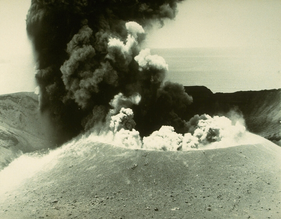 An ash plume erupting from the cone in the summit crater of Anak Krakatau on 2 May 1961. Anak Krakatau was in almost continuous activity from December 1959 until 1963. The newly formed cone displaced a lake that had filled the crater prior to the start of the eruption. Photo by D. Hadikusumo, 1961 (Volcanological Survey of Indonesia).