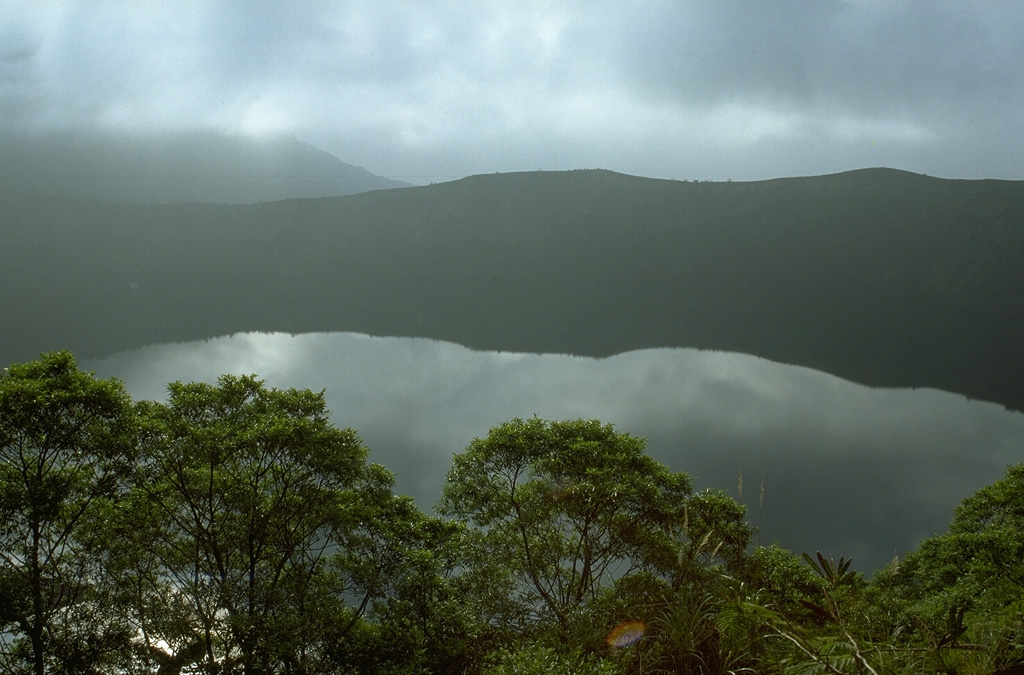 More than a decade after the powerful 1982-83 explosive eruption from Galunggung, the Warirang crater is filled by a lake that covers a late-stage scoria cone emplaced in the crater. A tunnel was constructed to stabilize the lake level and prevent overtopping and catastrophic breaching of the crater rim. Photo by Lee Siebert, 1995 (Smithsonian Institution).