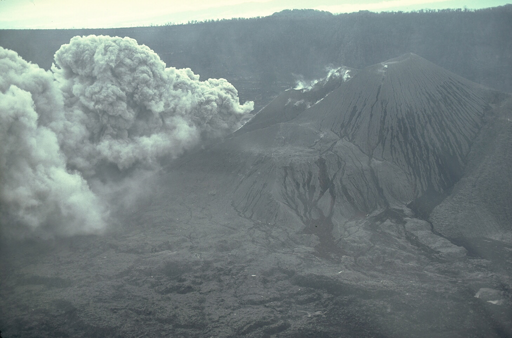 A new vent on the floor of Karkar's inner caldera began erupting on 12 January 1979. On 8 March a major phreatic eruption from the vent produced a directed explosion that devastated an area on the southern caldera rim. The explosion enlarged the January crater to a diameter of 300 m and a depth of 200 m. This 17 April view from the NE shows a low ash plume rising from the new crater. Photo by William Melson, 1979 (Smithsonian Institution)