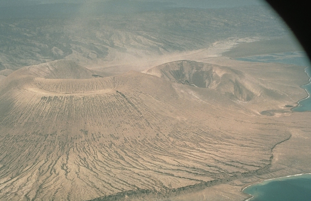 Vulcan, seen here from the SE, was the source of the largest eruptions at Rabaul in 1994. Vulcan began erupting on 19 September from a N-flank vent. Activity intensified rapidly, producing a large eruption column that reached an altitude of 20 km. Pyroclastic flows traveled radially down the flanks of the cone as far as 3 km and resulted in darkness in Rabaul city. The eruption originated from a N-S-trending fissure, seen here at the right. The scarp in the foreground was produced by a 5-m uplift the day before the eruption. Photo by Elliot Endo, 1994 (U.S. Geological Survey).