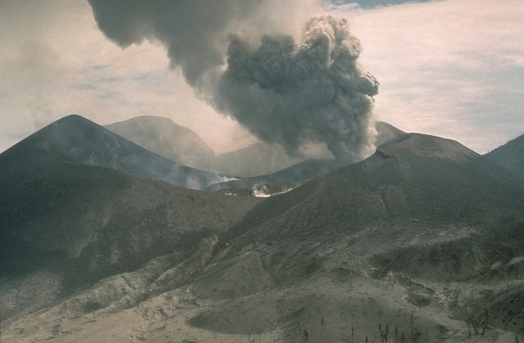 Lava in the center of the crater of Tavurvur volcano on 7 October 1994 as an ash plume rises from a vent to the E. Impact craters from volcanic bombs ejected by the volcano can be seen in the foreground on the flanks of the cone. Explosive eruptions from Tavurvur began on 19 September. Ash plumes initially reached a maximum height of 6 km, although typical heights were 1-2 km. A small lava flow was first seen in the summit crater of Tavurvur on 30 September. Photo by Andy Lockhart, 1994 (U.S. Geological Survey).