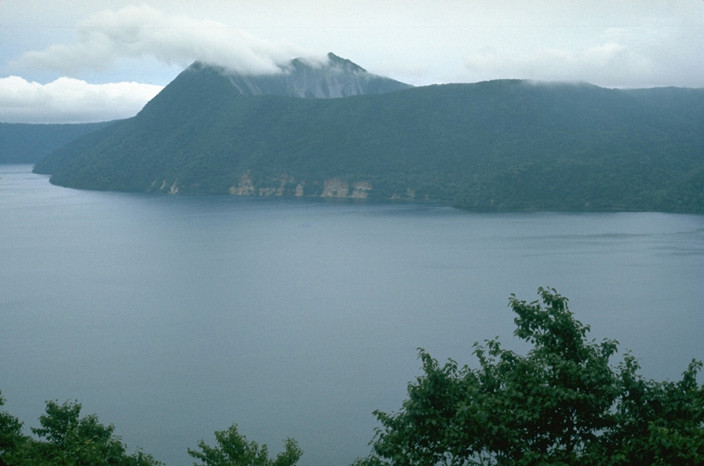 Kamuinupuri is a small cone on the SE rim of Mashu caldera. Growth of Kamuinupuri post-dated the roughly 7,000-year-old caldera collapse. The steep scarp below the summit is the NE wall of a 1.2 x 1.5 km caldera that formed at the summit about 1,000 years ago. Photo by Lee Siebert, 1977 (Smithsonian Institution).