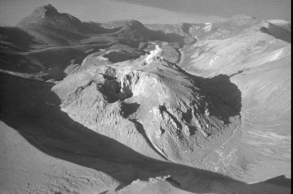 Berg volcano, seen here from the SE, is part of a closely spaced group of Holocene volcanoes in central Urup Island that is named after the most prominent cone, Kolokol. Berg has a 2-km-wide caldera that opens towards the NW and contains a large lava dome which was the most recently active of the group when this photo was taken in 1990. A small plume rises from an explosion crater on the NW side of the 250-m-high lava dome and a crater (center) is visible on the southern side. Eruptions have been documented since the late-18th century. Photo by A. Samoluk, 1990 (courtesy of Genrich Steinberg, Institute for Marine Geology and Geophysics, Yuzhno-Sakhalinsk).