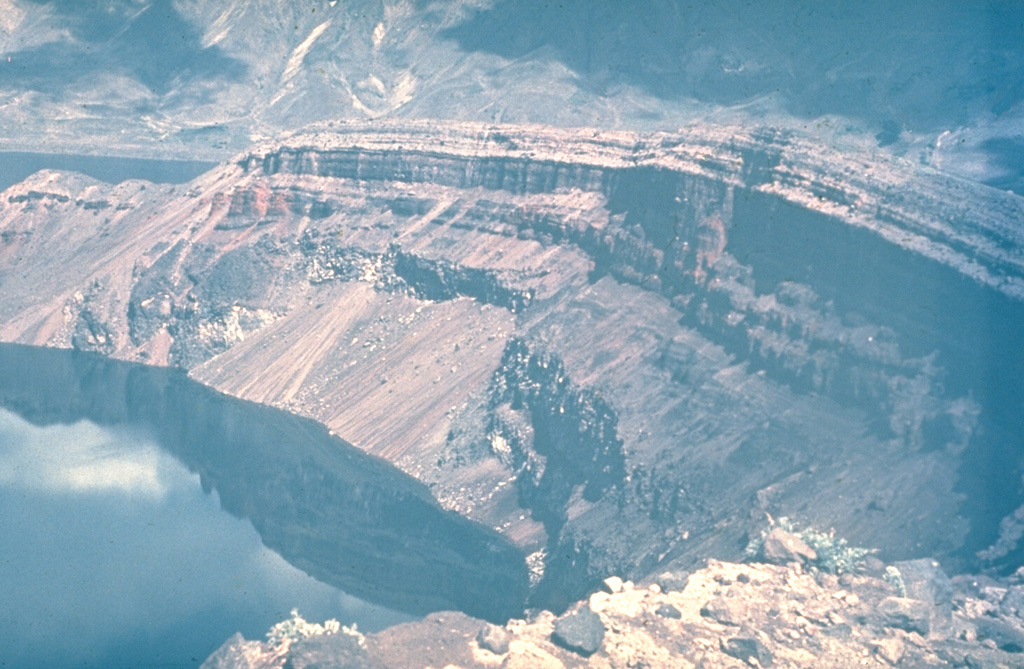 The NE wall of the Ksudach Shtyubel' crater is capped by bedded layers of tephra fall, pyroclastic flow, and pyroclastic surge deposits from the 1907 eruption. Three craters, 1.5, 0.6, and 0.4 km wide, formed along a NE-SW line. The eruption reduced the height of Shtyubel' cone by about 650 m and Shtyubel' lake filled the craters. The NE wall of Ksudach V caldera, inside which Shtyubel' cone was constructed, is visible at the top of the photo.  Photo by Yuri Doubik (Institute of Volcanology, Petropavlovsk).