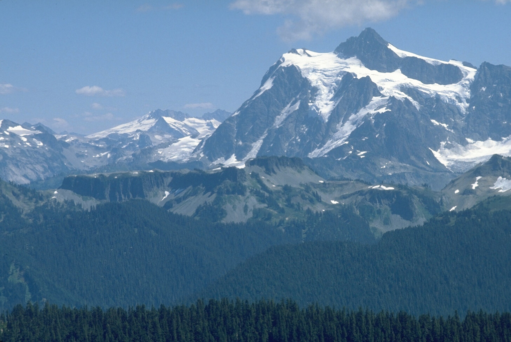 The flat-topped ridge in the center of this photo is Table Mountain, seen here from Skyline Divide. Table Mountain is a stack of andesitic lava flows, each about 100 m thick, that erupted from vents along the northern side of the Pleistocene Kulshan caldera. The buried northern caldera rim lies near the left-hand margin of the lava flows. The spectacular glacier-clad slopes of Mt. Shuksan form the right horizon, and Icy Peak at the head of the North Fork Nooksack drainage lies beyond it on the left-center horizon. Photo by Lee Siebert, 1979 (Smithsonian Institution).