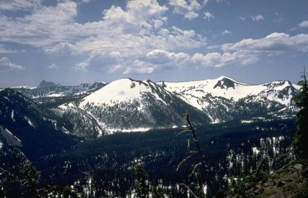 Snow-covered Forked Butte scoria cone in the center of the photo rises above the valley floor across from Bear Butte on the NE. A lava flow that was emplaced about 6,500 years ago can be seen down the left flank of the cone, one of two lobes that split around either side of Sugar Pine Ridge to the far left. Photo by Willie Scott, 1972 (U.S. Geological Survey).