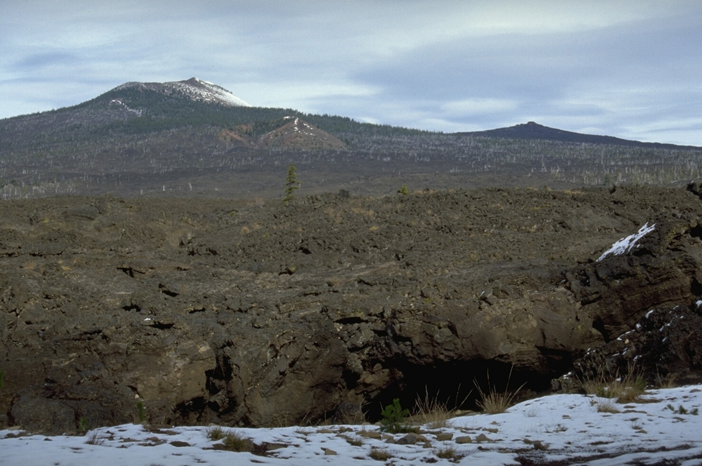 Lava flows in the foreground originated about 1,500 years ago from the South Belknap scoria cone below the skyline near the center of this photo. South Belknap scoria cone lies below Belknap Crater, a cone on the Belknap shield volcano. The lower peak on the right skyline is Little Belknap, a shield volcano constructed on the E flank of Belknap. Largely unvegetated lava flows cover nearly 100 km2 in the McKenzie Pass area. Photo by Lee Siebert, 1995 (Smithsonian Institution).