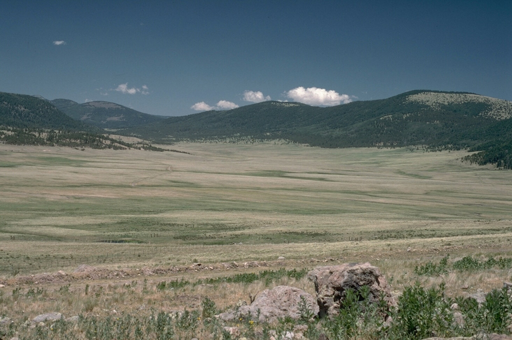 The 22-km-wide Valles caldera in northern New Mexico was formed during a series of major eruptions ending with the eruption of the Bandelier Tuff about 1 million years ago.  Post-caldera uplift formed a large resurgent dome in the center of the caldera.  The latest eruptions occurred about 130,000 years ago, but geothermal activity continues.  This view from the caldera moat shows the rim of the 1.45 million-year-old Toledo embayment to the north, with the edge of the Cerro del Medio rhyolitic lava dome at the extreme left. Photo by Lee Siebert, 1989 (Smithsonian Institution).