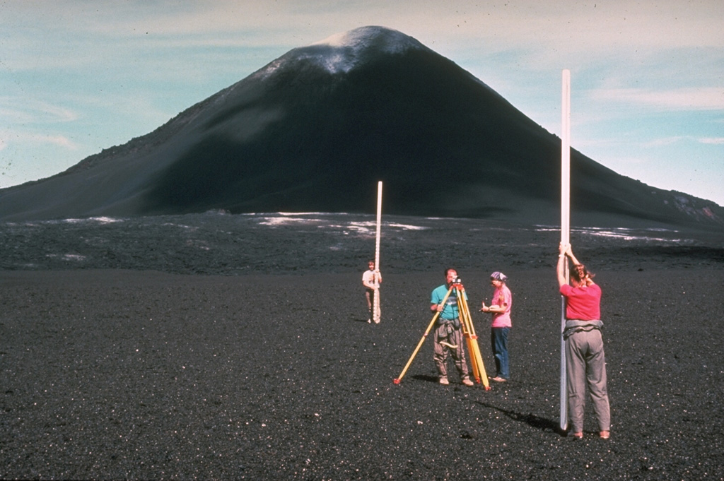 Among the many monitoring techniques used by Hawaiian Volcano Observatory staff at Kilauea volcano is precision leveling. Millimeter-scale changes can be detected with an optical-level instrument by measuring the precise difference in elevation on leveling rods placed above two fixed points. Slight changes in the shape of a volcanic edifice commonly occurs prior to eruptions. Measurements such as these in 1968, with the Puʻu ʻŌʻō scoria cone in the background, are one of several techniques used to help forecast eruptive events. Photo by Richard Fiske, 1986 (Smithsonian Institution).