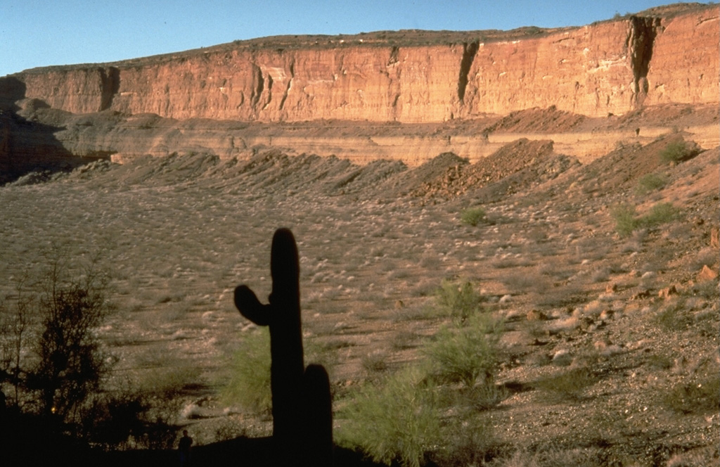 The Cerro Colorado maar, in the Pinacate volcanic field 24 km NE of Pinacate Peak, contains a 1-km-wide crater formed by explosions on a nearly flat surface. Distribution of ejecta by prevailing winds produced a hill on the side of the crater opposite this steep, 110-m-high crater wall. The ejecta include fragments of underlying granitic and metamorphic rocks. Photo by Richard Waitt, 1988 (U.S. Geological Survey).