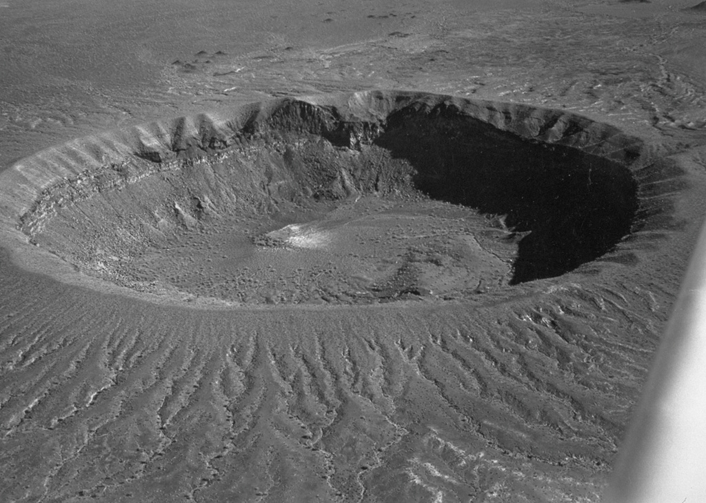 Cráter Elegante, seen here in an aerial oblique view from the NW, is a 1.6-km-wide maar in the Pinacate volcanic field. Within the crater walls are exposed basaltic lava flows, sills, and dikes pre-dating formation of the maar, which are overlain by pyroclastic surge deposits that cover the rim and outer flanks. Lake beds within the maar have been radiocarbon dated at between about 13,000 and 17,000 years, indicating a late-Pleistocene age for the maar-forming eruptions. Photo by David Roddy, 1965 (U.S. Geological Survey).