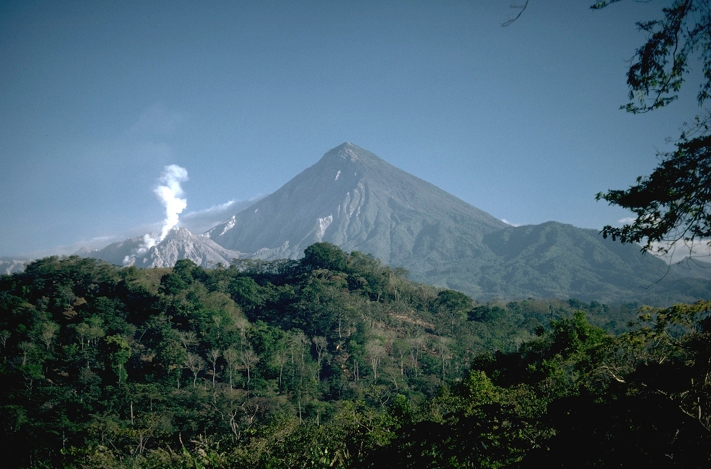 Three distinct stages marked the growth of Santa María. The large edifice formed over a basement of older volcanic and plutonic rocks beginning about 30,000 years ago and ending about 500 to several thousand years ago. A massive eruption in 1902 then created the large crater on the SW flank seen in the shadow left of the summit. The third stage is marked by continued growth of the Santiaguito lava dome complex (left) in the new crater since 1922. Photo by Lee Siebert, 1988 (Smithsonian Institution).