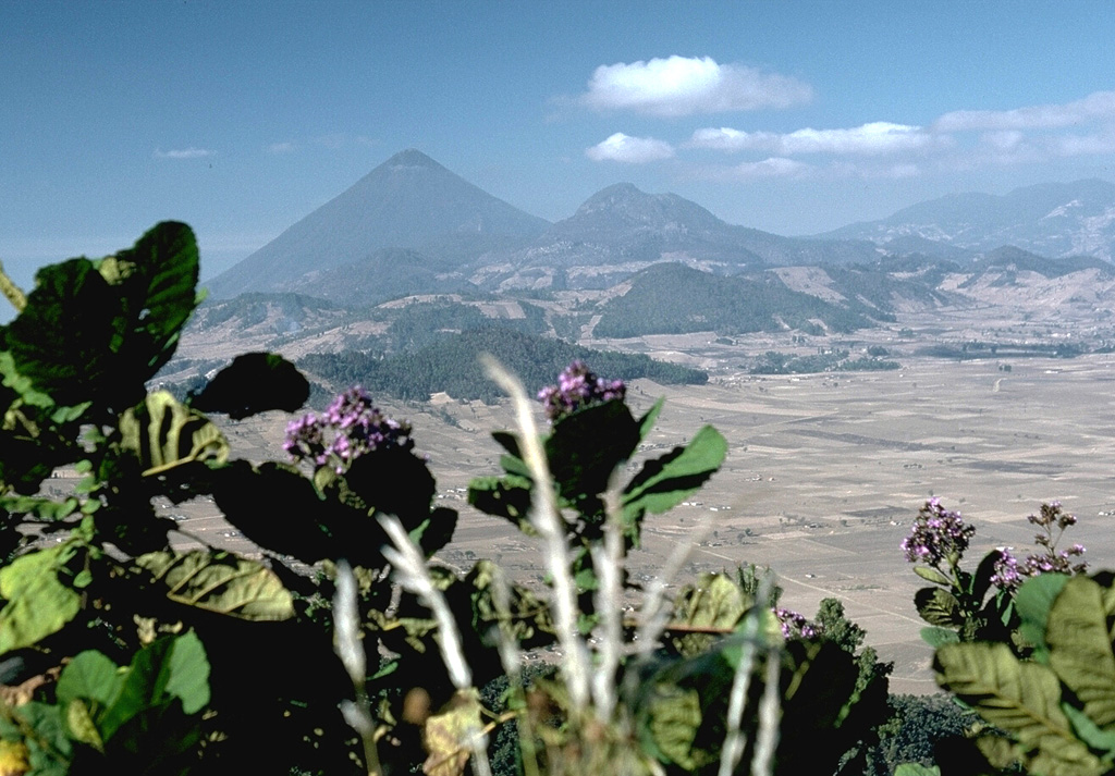 The rounded hills in the middle of the photo are part of a chain of lava domes of the Almolonga volcanic field. Partial flank collapse of an edifice sometime prior to 84,000 years ago formed a 3.3-km-wide collapse scarp that is surrounded by a ring-dike configuration of dacite and rhyolite lava domes, seen here from the east. Cerro Quemado is a young dome near the center of the horizon, right of the larger Santa María, that produced a 2.5-km-long lava flow on its eastern flank in 1818. Photo by Lee Siebert, 1988 (Smithsonian Institution).