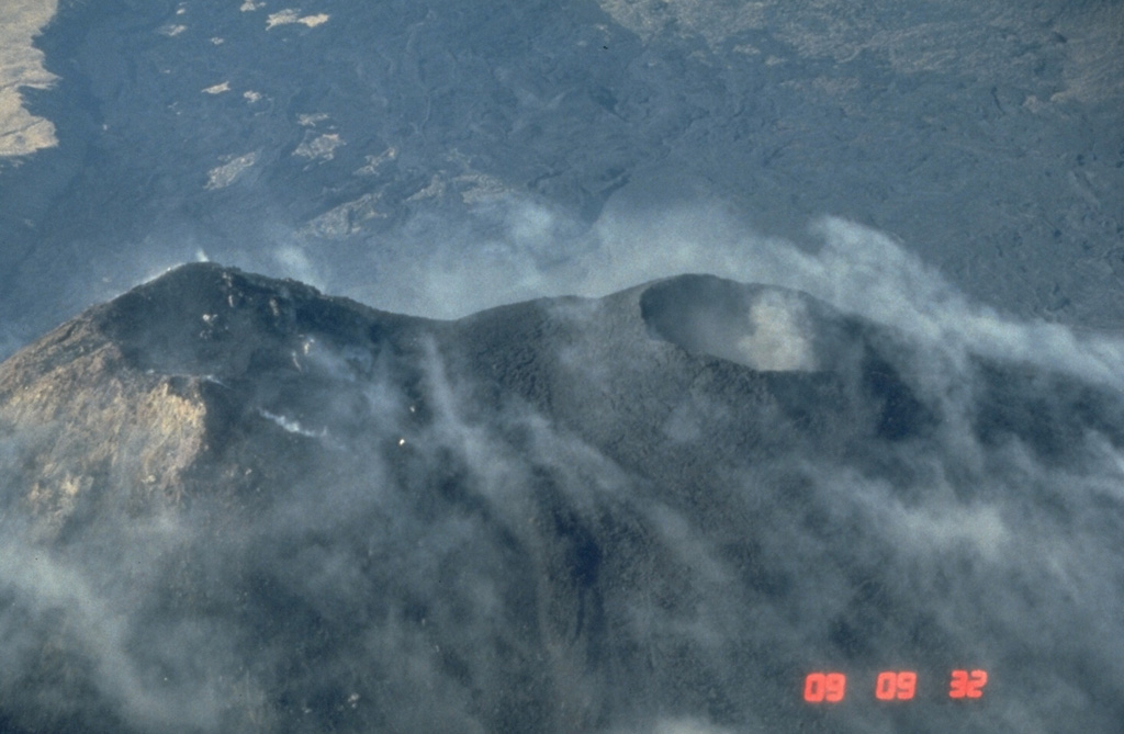 MacKenney crater (right), constructed NW of an older cone at the left, has been the source of most of Pacaya's historical eruptions. Frequent Strombolian eruptions repeatedly build up the cone after it is partially destroyed by intermittent larger explosions. An extensive lava flow field produced from MacKenney cone since 1965 is in the background of this 25 January 1987 view from the NE. Photo by Norm Banks, 1987 (U.S. Geological Survey).