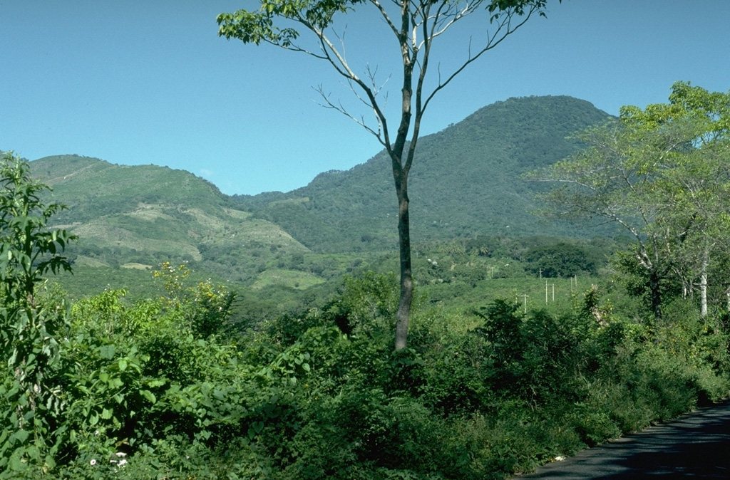 The low ridge on the left-hand horizon is the southern rim of a large horseshoe-shaped crater left by collapse of Miraflores, an ancestral edifice of the Tecuamburro volcanic complex. Miraflores formed about 100,000 years ago and collapsed sometime prior to 38,000 years ago. The vegetated peak to the right is part of the Tecuamburro lava dome complex, which formed within the scarp. Photo by Lee Siebert, 1988 (Smithsonian Institution).