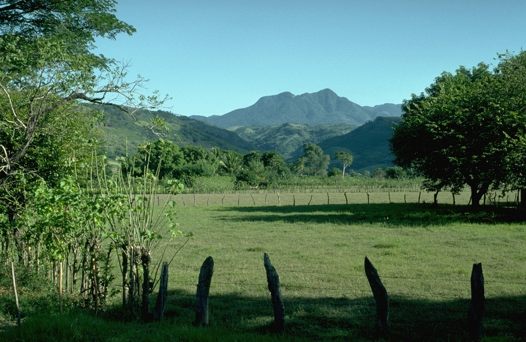 Moyuta rises above farmlands on the Pacific coastal plain of Guatemala. The forested volcano is extensively eroded and is mostly Pliocene and Pleistocene, but has a cluster of relatively young andesite to dacite lava domes at its summit. North-trending faults across the summit area form step-like ridges. Fumaroles, acid springs, and bicarbonate-rich hot springs are located on the northern and southern flanks. Photo by Lee Siebert, 1988 (Smithsonian Institution).