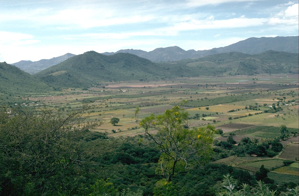 The floor of the 5-km-wide Retana caldera between Suchitán and Tahual volcanoes is now used for farmland. The caldera walls range up to 250 m in height, with a low notch on the northern rim (left).  Photo by Lee Siebert, 1993 (Smithsonian Institution).