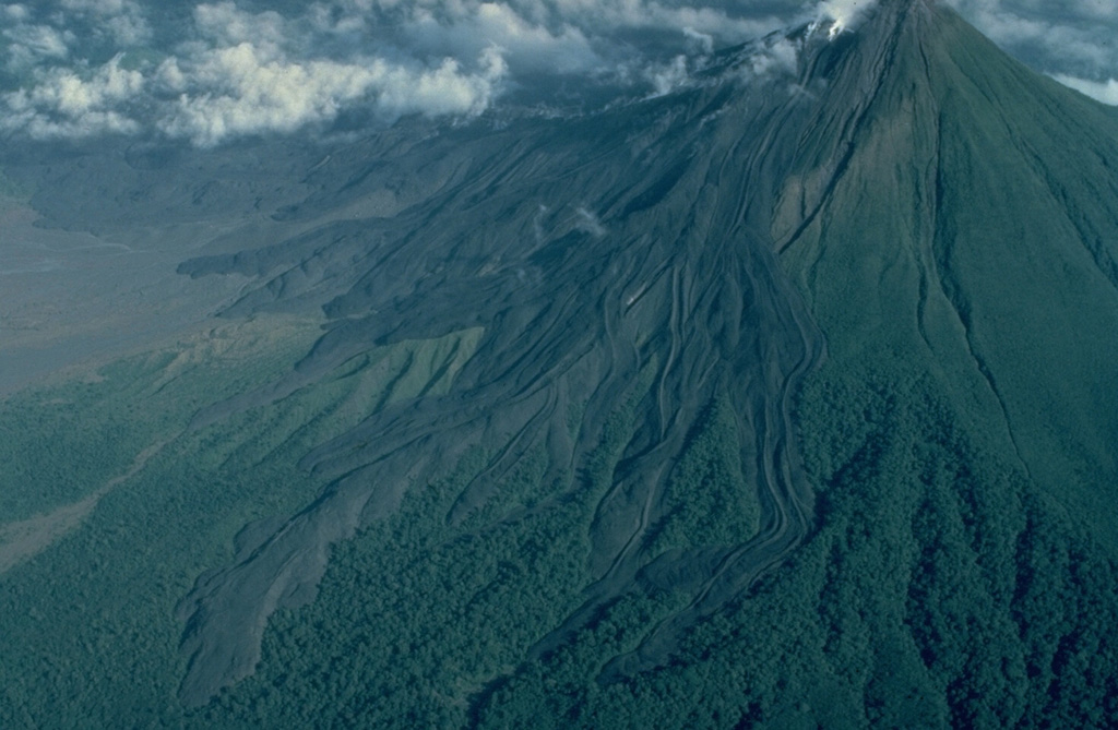 Lava flows armor the western flank of Arenal volcano in Costa Rica.  All the flows seen here were emplaced during a long-term eruption that began in 1968.  This 1983 aerial view from the SSW shows many individual lava-flow lobes.  Prominent flow levees are visible, particularly on the flows at the right.  Lava flows from the current Arenal eruption extend 4 km to the NW and about 2.5 km to the SW. Copyrighted photo by Katia and Maurice Krafft, 1983.