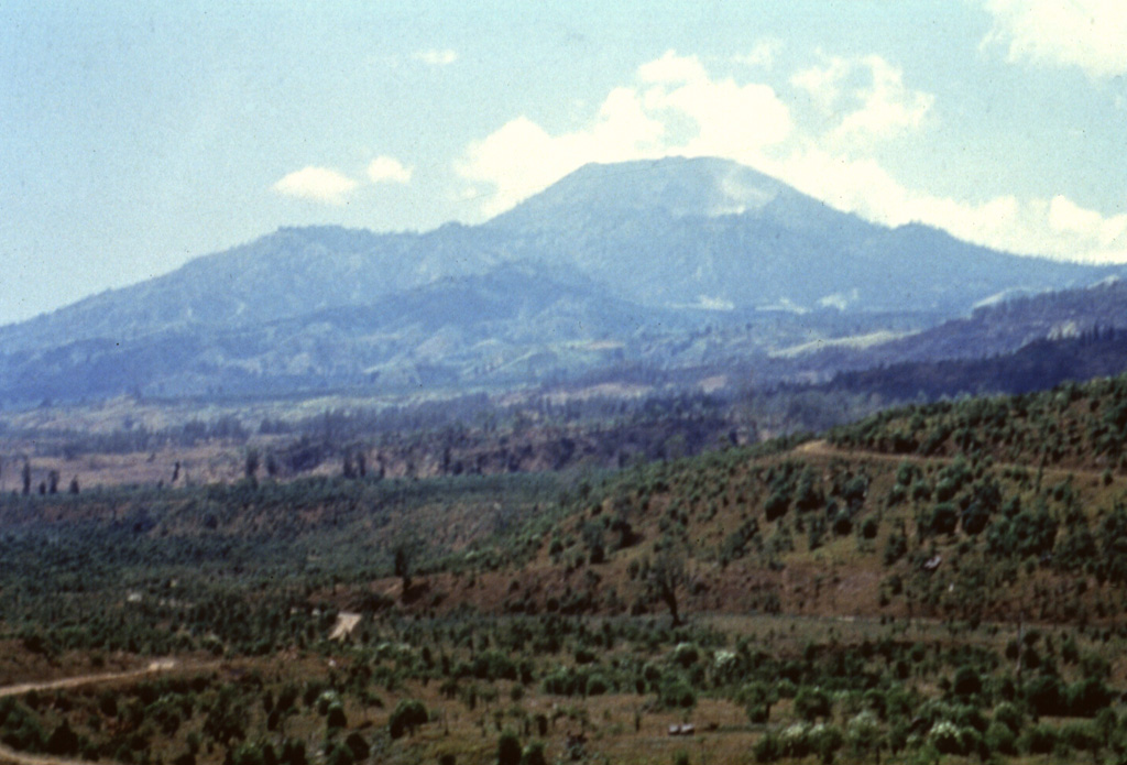 Tangkuban Parahu seen here from the E, forms the most prominent peak N of the city of Bandung. The summit overlooks a broad crater complex, whose southern rim forms the flat ridge left of the summit. Pyroclastic-flow deposits emplaced during the formation of a large caldera that preceded the construction of Tangkubanparahu are present around Bandung. Anonymous, 1991.