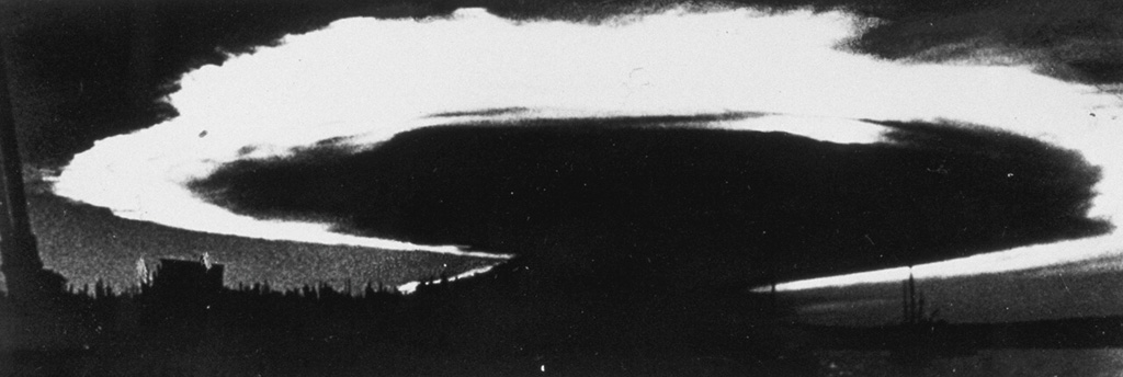 Caldera collapse in 1968 at the basaltic shield volcano, Fernandina, was preceded by lava effusion on the SE flank and a major explosive eruption on 11 June. The ash plume, seen here from Academy Bay on Santa Cruz Island within minutes of the explosion, is backlit by the late afternoon sun and was spreading at an estimated lateral speed of 80 km per hour. At the time of this photograph the ash plume was 175 km across with an altitude of 20-25 km. Photo by J. Harte, 1968 (published in Simkin and Howard, 1970).