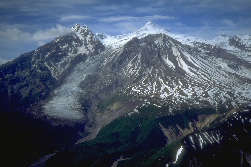 During the late Pleistocene or early Holocene Mount Spurr underwent flank collapse, resulting in the 5-6 km crater that opens to the south shown here in 1993. The collapse produced a debris avalanche that traveled at least 25 km from the summit. The snow-covered peak (center) is a post-collapse lava dome. Crater Peak, in front of it, has been the source of frequent Holocene eruptions. Photo by Christina Neal, 1993 (U.S. Geological Survey, Alaska Volcano Observatory).