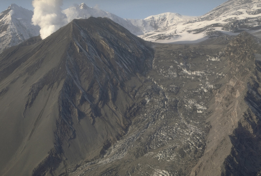 The last of three brief 1992 explosive eruptions at the Crater Peak vent of Mount Spurr showered hot debris onto the Kidazgeni Glacier immediately east of the cone. In this 23 September view, six days after the end of the eruption, a plume rises from Crater Peak and dark pyroclastic material covers the flanks of the cone and adjacent glacial ice. Photo by Cynthia Gardner, 1992 (U.S. Geological Survey).