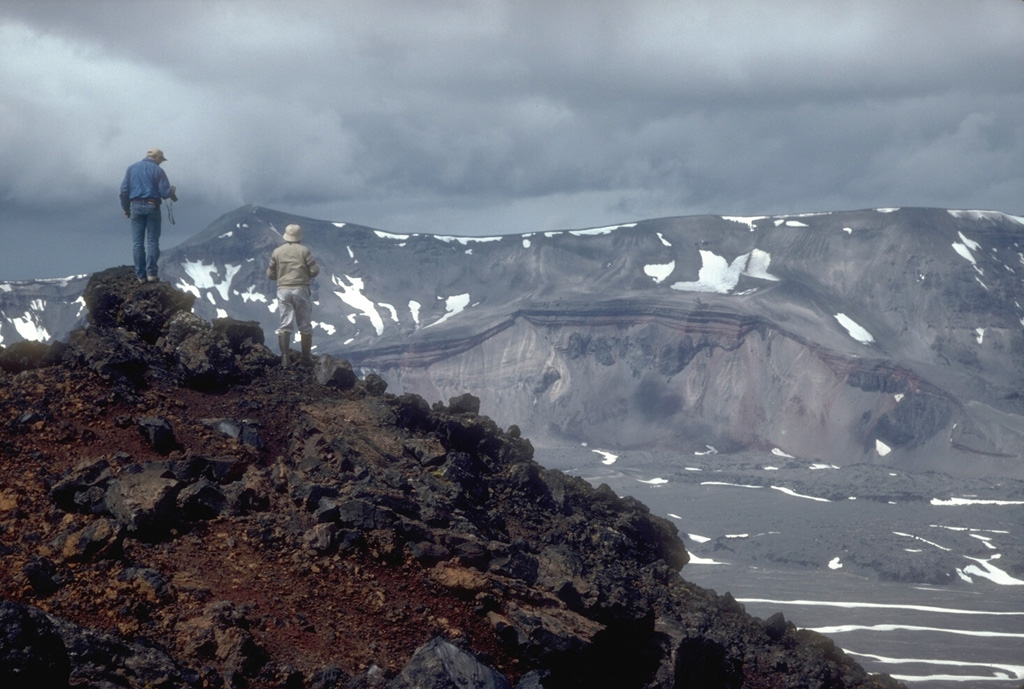 Volcanologists from the U.S. Geological Survey on the rim of the intra-caldera Vent Mountain at Aniakchak look NW towards Half Cone, a prominent feature on the caldera floor and the source of an explosive post-caldera eruption. The NW caldera rim of Aniakchak caldera forms the skyline. Photo by Christina Neal, 1992 (Alaska Volcano Observatory, U.S. Geological Survey).