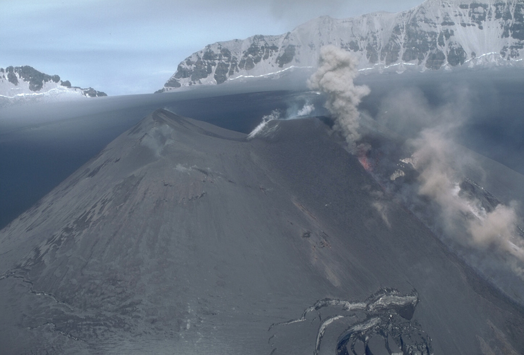 Ash and incandescent lava fragments rise above a fissure on a scoria cone at the summit of Veniaminof on 13 July 1983. The eruptions began on 2 June and covered the cone and much of the caldera floor with ash. Note the ash-covered glacial crevasses on the flanks of the cone to the lower right. The rim of the 8 x 11 km caldera appears in the distance to the NE. Photo by Betsy Yount, 1983 (Alaska Volcano Observatory, U.S. Geological Survey).