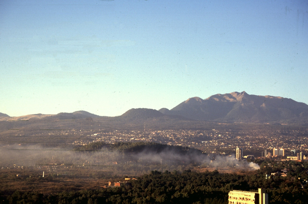 The Xitle scoria cone, the large flat-topped cone on the center horizon, is one of the youngest features of the Chichinautzin volcanic field. Xitle erupted about 1,670 years ago. Initial ash emission was followed by extrusion of a lava flow that traveled 13 km N and covered the prehistoric Cuicuilco urban centers and nearby agricultural lands. Portions of Mexico City, including the National University (UNAM), were built on this lava flow. The Ajusco lava-dome complex appears to the upper right. Photo by Gerardo Carrasco-Núñez, 1997 (Universidad Nacional Autónoma de México).