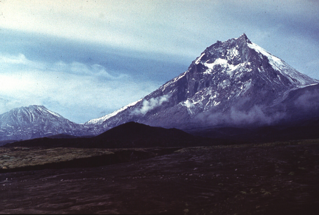 Kamen lies at the center of a N-S-trending chain of volcanoes, flanked by Bezymianny (left) and Klyuchevskoy. Kamen formed during the late Pleistocene and activity continued into the Holocene. A major flank collapse about 1,200-1,300 years ago removed much of the eastern side of the volcano, leaving the steep escarpment seen in this view. Photo by Vera Ponomareva, 1975 (Institute of Volcanic Geology and Geochemistry, Petropavlovsk).