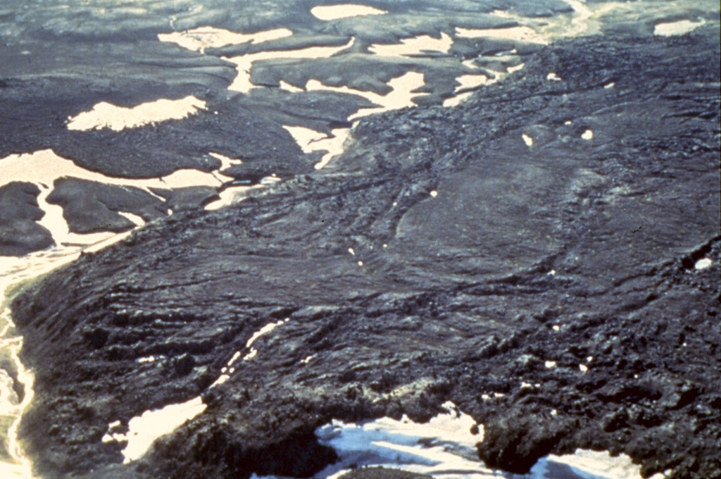 The silicic Hrafntinnuhraun eruption occurred in about 877 CE, producing about 0.18 km3 of lava and 0.4 km3 of tephra. An eruption column of up to 20 km high was associated with this Plinian eruption. The Hrafntinnuhraun lava flow stretches from the bottom left to top right in this image, with a stream running around its base on the left reflecting the sun. Photo by Richie Williams, 1981 (U.S. Geological Survey).