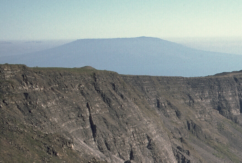 Cerro Azul volcano at the SW tip of J-shaped Isabela Island rises in the distance above the rim of Fernandina caldera.  The flat-topped shield volcano is truncated by a deep, steep-walled 4 x 5 km summit caldera.  A prominent cinder cone is located at the ENE side of the caldera and youthful lava flows cover its floor.  Numerous spatter cones dot the western flanks.  Fresh-looking lava flows, many erupted from circumferential fissures, descend the NE and NW flanks.  Historical eruptions date back only to 1932.      Photo by Lee Siebert, 1978 (Smithsonian Institution).