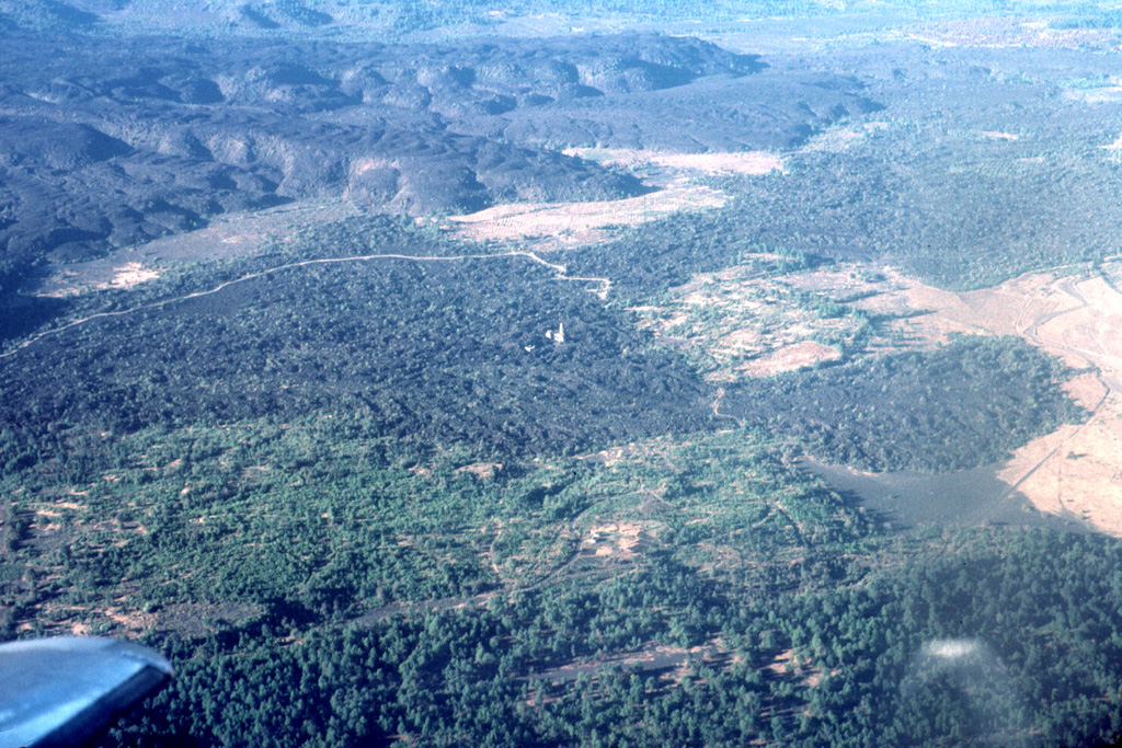 The small light-colored spire in the center of the photo is the renowned steeple of the church of San Juan Parangaricutiro, which was surrounded by lava flows from Parícutin volcano in 1944 in this view from the NE. The steep-sided, viscous lava flows in the background were erupted later, during 1944-46. This is one of numerous lava flows within the Michoacan-Guanajuato volcanic field. Photo by Jim Luhr, 1997 (Smithsonian Institution).