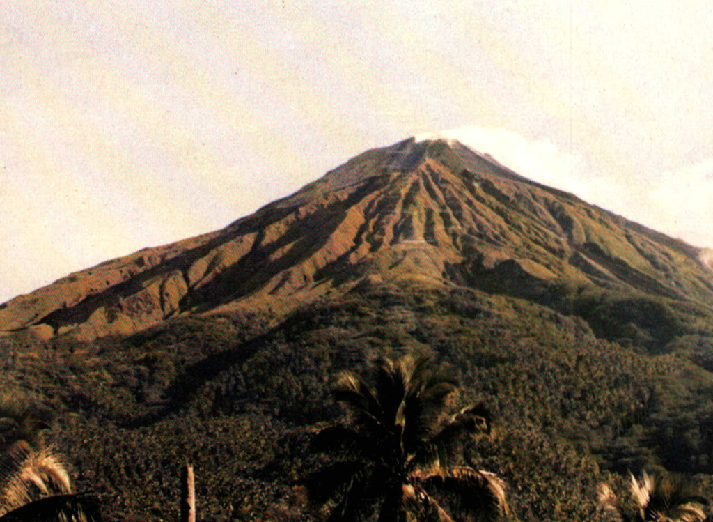 Karangetang (Api Siau) volcano rises above the Pengamatan Maralawa volcano observation post of the Volcanological Survey of Indonesia near the village of Salili on the southern flank.  Karangetang is one of Indonesia's most active volcanoes.  Twentieth-century eruptions have included frequent explosive activity that is sometimes accompanied by pyroclastic flows and lahars.  Lava dome growth has occurred in the summit craters; collapse of lava flow fronts has also produced pyroclastic flows.   Photo by L. Manalu, 1986 (Volcanological Survey of Indonesia).