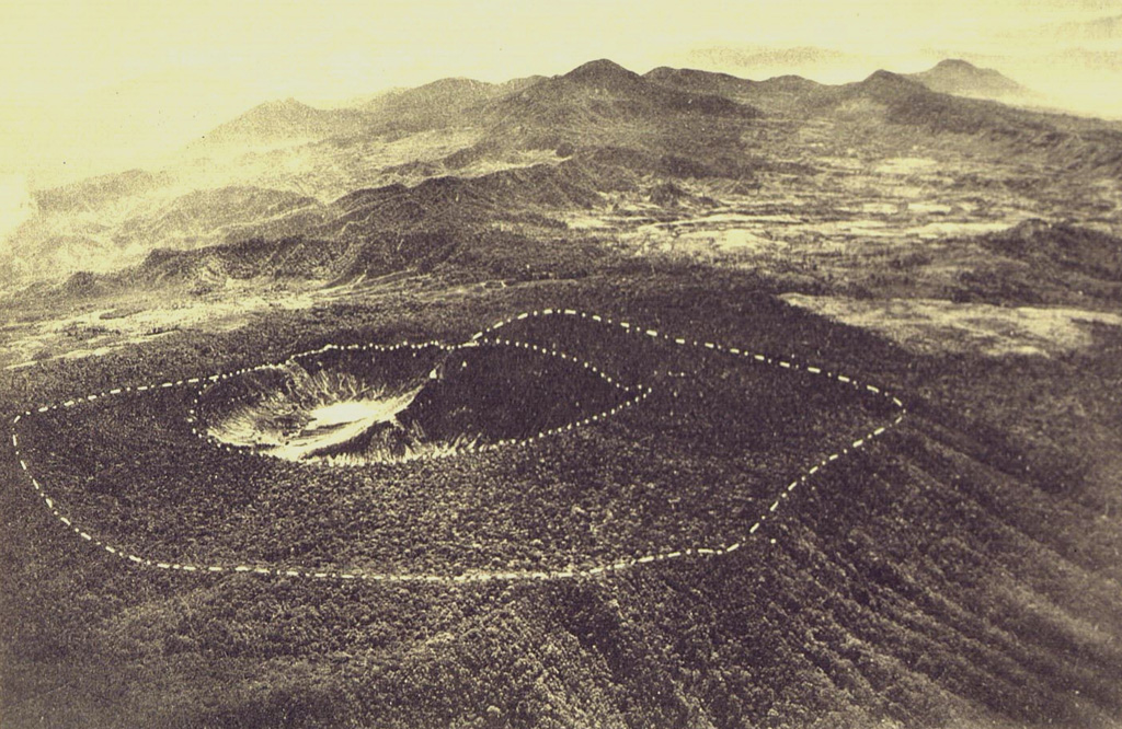 The broad summit of Tangkuban Parahu volcano is seen in this aerial view from the NW. The dashed line outlines an outer crater inside which a younger crater complex (dotted line) was constructed. Frequent phreatic eruptions have occurred during historical time from the central crater complex. Bukit Tunggul, an older volcano is the peak visible at the center of the horizon. Photo published in Taverne, 1926 