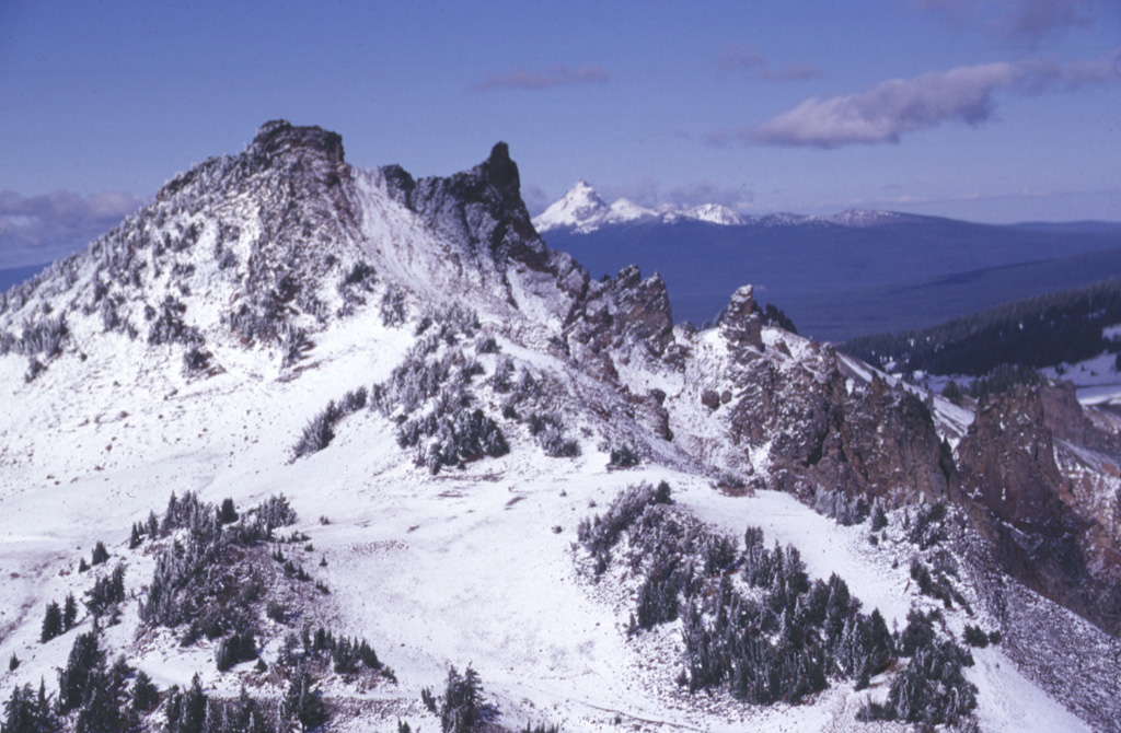 Hillman Peak, the westernmost andesitic stratovolcano of Mount Mazama, is partially dissected by Crater Lake caldera. The base of the cone consists of thin andesite lava flows; these are overlain by bedded fall deposits. The upper part of the cone, seen here, consists of andesitic lava flows erupted about 67,000 years ago. The snow-capped peak on the far horizon to the north is Mount Thielsen, a Pleistocene volcano. Photo by Lee Siebert, 1997 (Smithsonian Institution)