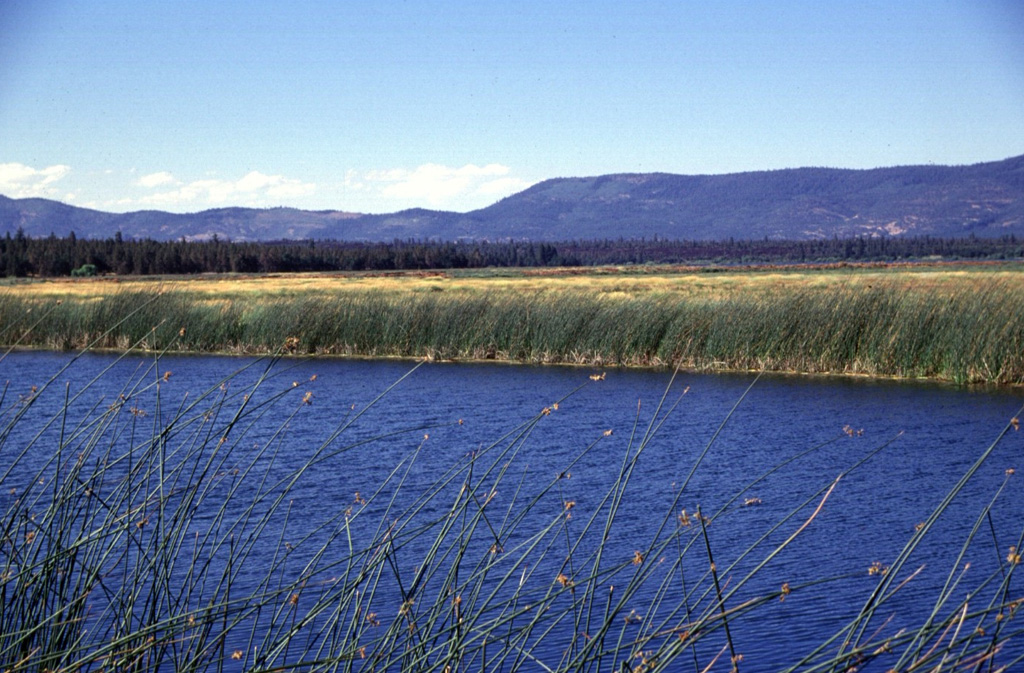 A series of lava flows erupted from Brushy Butte volcano form the dark forested line extending across the photo below the Big Valley Mountain fault scarp in the background.  Lava Springs State Park north of the town of MacArthur marks the location of numerous springs that issue from the margin of the Brushy Butte lava flows to form Big Lake, the Little Tule River, and Falls River. Photo by Lee Siebert, 1998 (Smithsonian Institution).