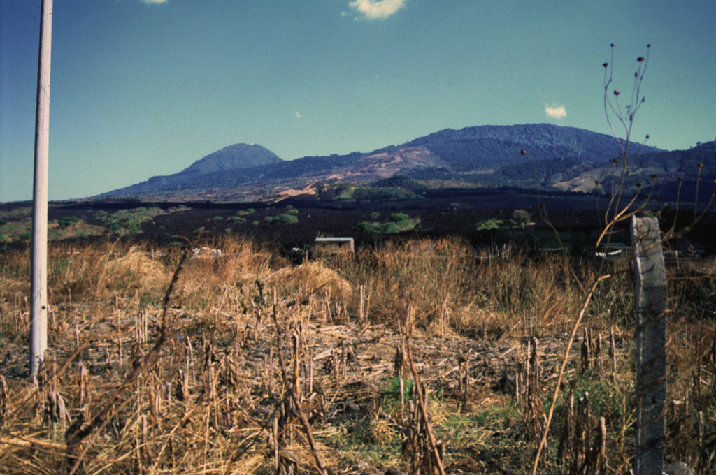 The dark-colored lava flow in the center of the photo originated during an eruption in 1917 from a vent high on the northern flank of Boquerón volcano (upper right).  On June 6, 1917 an eruption began from NW-trending fissures on the upper north flank of Boquerón.  A chain of cinder cones formed and a lava flow traveled to the northwest, cutting the railroad between Quezaltepeque and Sitio del Niño.  Eruptive activity also occurred at the summit crater of Boquerón, where a small conelet formed on the crater floor.  El Picacho peak is at the left. Photo by Giuseppina Kysar, 1999 (Smithsonian Institution).