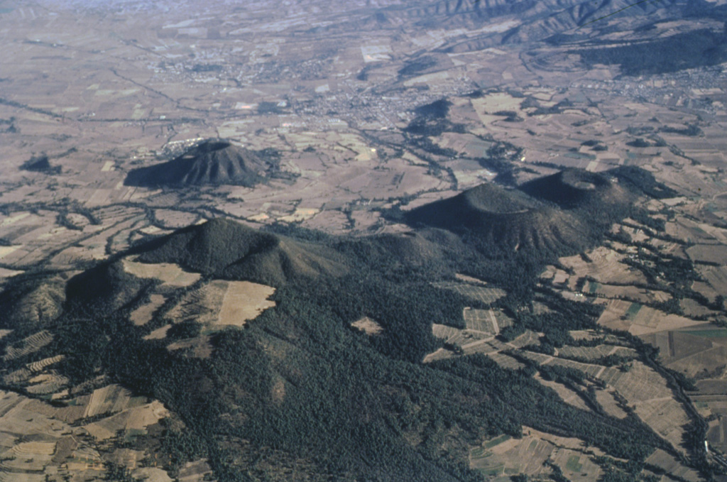 Five small scoria cones are aligned NE-SW near the town of Amecameca at the far eastern end of the Chichinautzin volcanic field. The large cone to the lower left is Cerro Chinconquiat, the larger of the two cones at the mid-right is Cerro Tapeixte, and the smaller one at the far right is Cerro la Joya. The cone with radian erosion gullies to the left immediately above Cerro Chinconquiat is Cerro Tenayo. Photo by José Macías, 1996 (Universidad Nacional Autónoma de México).