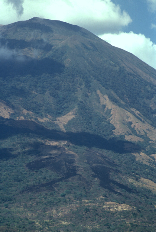 The dark-colored areas at the bottom of the photo are lava flows erupted from a SSE-flank vent of San Miguel in December 1855.  The larger dark area above it extending diagonally across the image is a cloud shadow.  The 1855 lava flows were erupted from a SSE-trending radial fissure and were the smallest flows erupted at San Miguel in historical time, extending only about a kilometer from the vent. Photo by Paul Kimberly, 1999 (Smithsonian Institution).