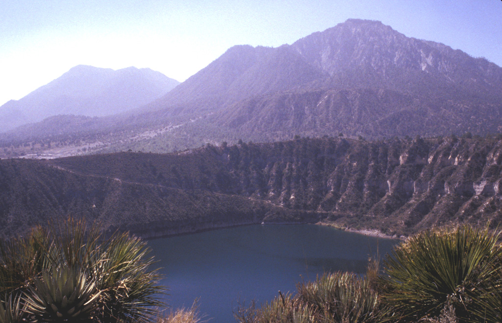 The Las Derrumbadas lava domes rise above the rim of the San Luis Atexcac maar. The two rhyolite lava domes rise about 1 km above their bases. The NW dome (right) consists of a microcrystalline rhyolite that has been extensively altered by fumarolic activity. The SE dome (left) is of similar lithology. The carapace of both domes has been removed by a series of slope failures. The San Luis Atexcac maar in the foreground erupted through Cretaceous limestones and Tertiary monzonites and hornfels. Photo by Lee Siebert, 1998 (Smithsonian Institution).