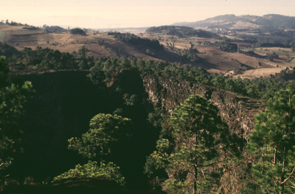 The steep-walled 200-m-wide crater in the foreground at El Volcancillo on the NE flank of Cofre de Perote was the source of the voluminous Río Naolinco lava flow about 900 years ago. The pahoehoe lava flow traveled initially to the north and then to the east for a distance of 50 km, partly within lava tubes. El Volcancillo consists of two overlapping craters constructed on a ridge crest. The Río Naolinco lava flow originated from the NW crater; the SE crater fed the Toxtlacuaya ‘a’a lava flow down a valley on the opposite side of the ridge. Photo by Lee Siebert, 1998 (Smithsonian Institution).