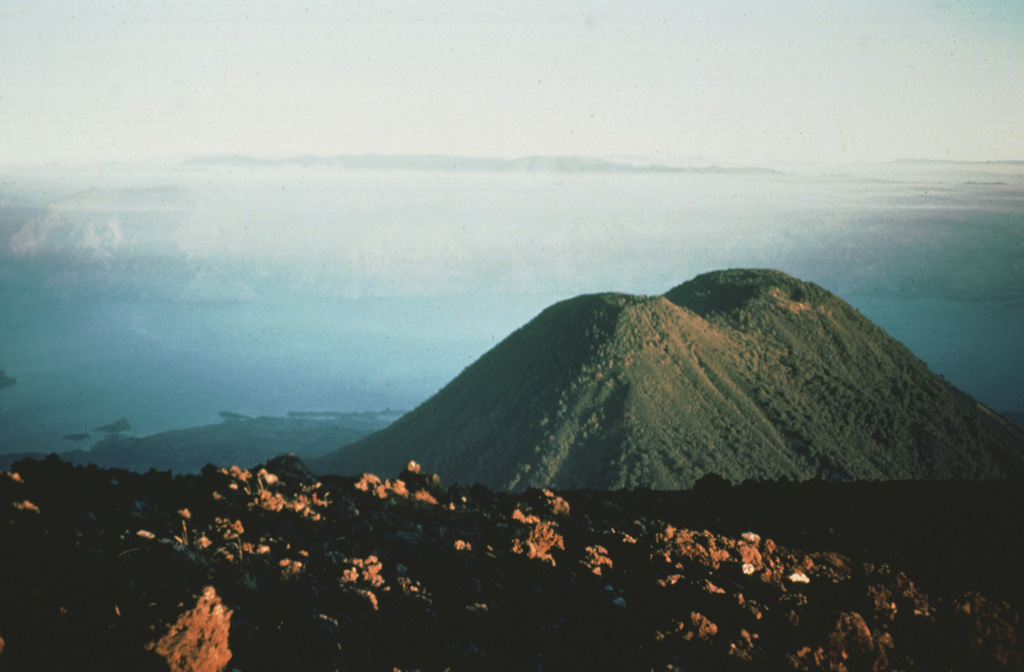 Tolimán volcano is 4 km away beyond the summit of Atitlán. Atitlán was constructed over the approximate rim of the Atitlán III caldera, whereas Tolimán was built over the margin of Atitlán II caldera. The irregular Lake Atitlán shoreline to the left is formed by lava flows from Tolimán. The far Atitlán III caldera rim can be faintly seen across the lake. The two post-caldera cones have dramatically different eruptive styles, with lava flows dominating at Tolimán and pyroclastic eruptions at Atitlán.  Photo by Bill Rose, 1983 (Michigan Technological University).