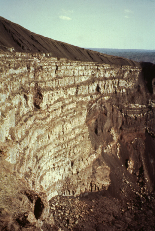 Santiago crater was initially formed in 1853, but the present pit crater formed during the 1858-1859 eruption.  A column of flames and ash eruptions were reported on January 27 and March 27, 1859 accompanied by collapse of Santiago and San Pedro Craters.  After its initial collapse, Santiago pit crater was a vertical cylinder about 150 m deep and 600 m across.  By the time of the 1865 visit of Seebach, the craters had evolved to their present configuration.  Photo by Jaime Incer, 1992.