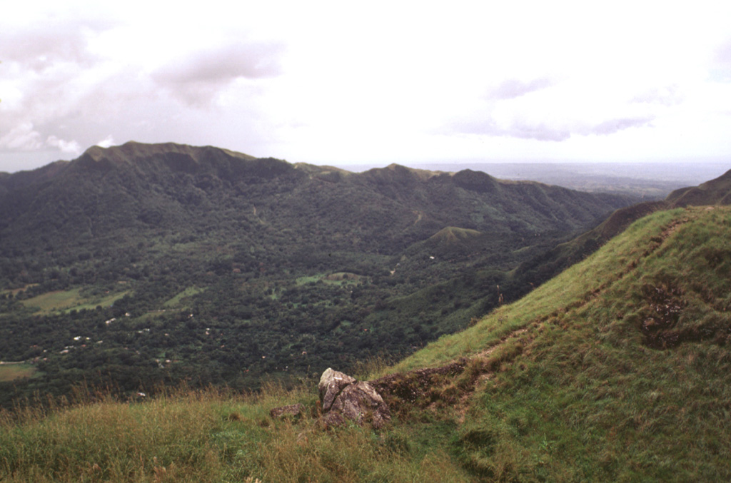 El Valle de Antón caldera (left) is seen here where a late-Pleistocene lake occupied the caldera floor and persisted until it drained sometime during the Holocene. Cerro Cara Iguana (upper left) on the caldera rim contains El Hato pyroclastic flow deposits from caldera formation about 1.1-1.3 million years ago. A crater just out of view outside the SW caldera rim at the right was the inferred source of the India Dormida ignimbrite that was erupted about 220,000 years ago.  Photo by Lee Siebert, 1998 (Smithsonian Institution).