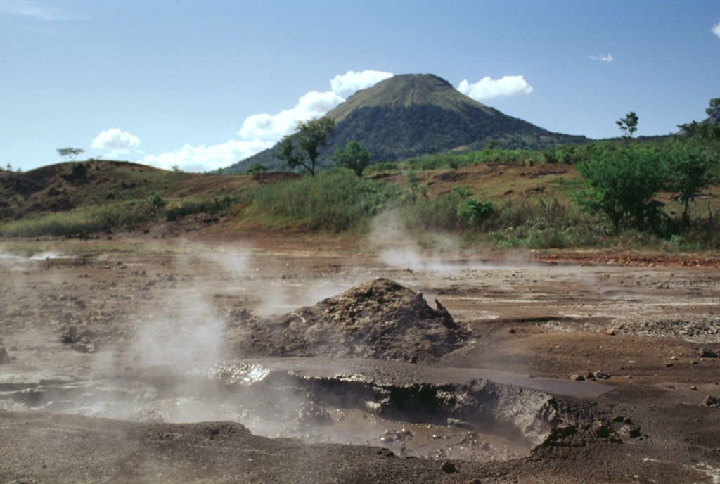 Mud pots and steaming vents of the San Jacinto thermal area lie at an elevation of 140 m at the eastern end of the Telica volcanic complex.  Thermal manifestations cover a broad area here and along a N-S-trending fault at Tizate, about 2 km to the NNE.  Conical Santa Clara volcano rises to 834 m in the background. Photo by Lee Siebert, 1998 (Smithsonian Institution).