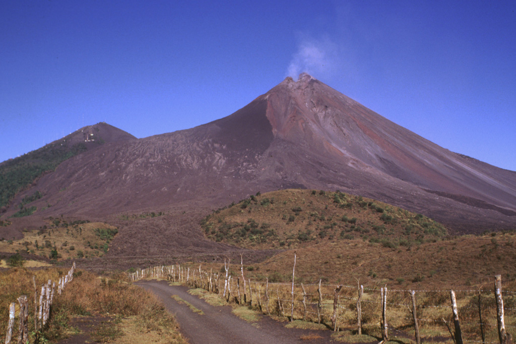 Lava flows were erupted in late 1998, seen across the upper left-hand flank of the degassing MacKenney cone at Pacaya in February 1999. They originated from vents at the summit and upper flanks of the cone and descended into the caldera before being deflected by the caldera wall to the west. The hill on the left horizon is Cerro Chino, a scoria cone constructed on the NW crater rim. Strong explosive eruptions in 1998 created a notch in the summit of MacKenney cone and the deep gully that extends diagonally down to the right. Photo by Lee Siebert, 1999 (Smithsonian Institution).